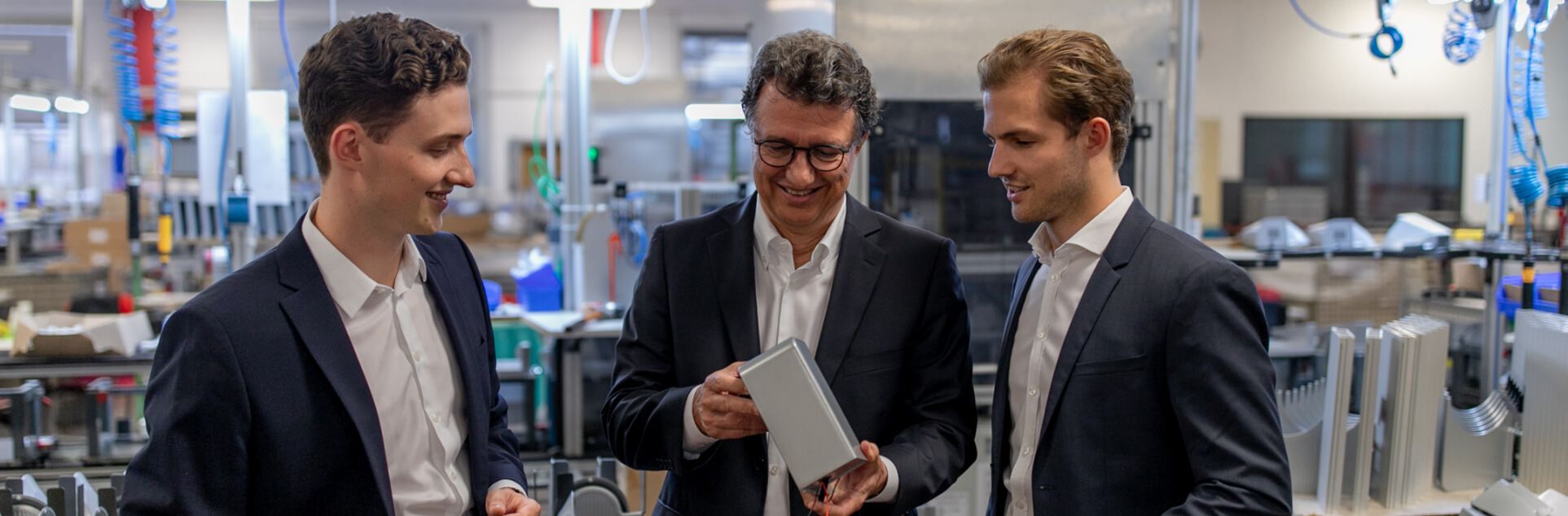 Ein Bild von drei Männern die in einer Werkstatt stehen und über etwas reden.