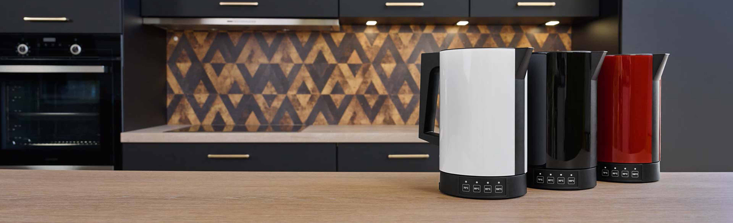 A picture of a red, a black and a white kettle standing next to each other on a kitchen platform.