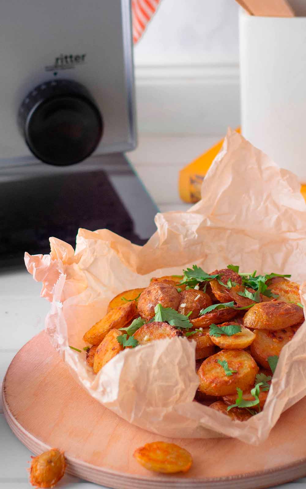 Knusprige Country Potatoes in Backpapier serviert, garniert mit frischer Petersilie. Im Hintergrund ist ein ritter Allesschneider zu sehen
