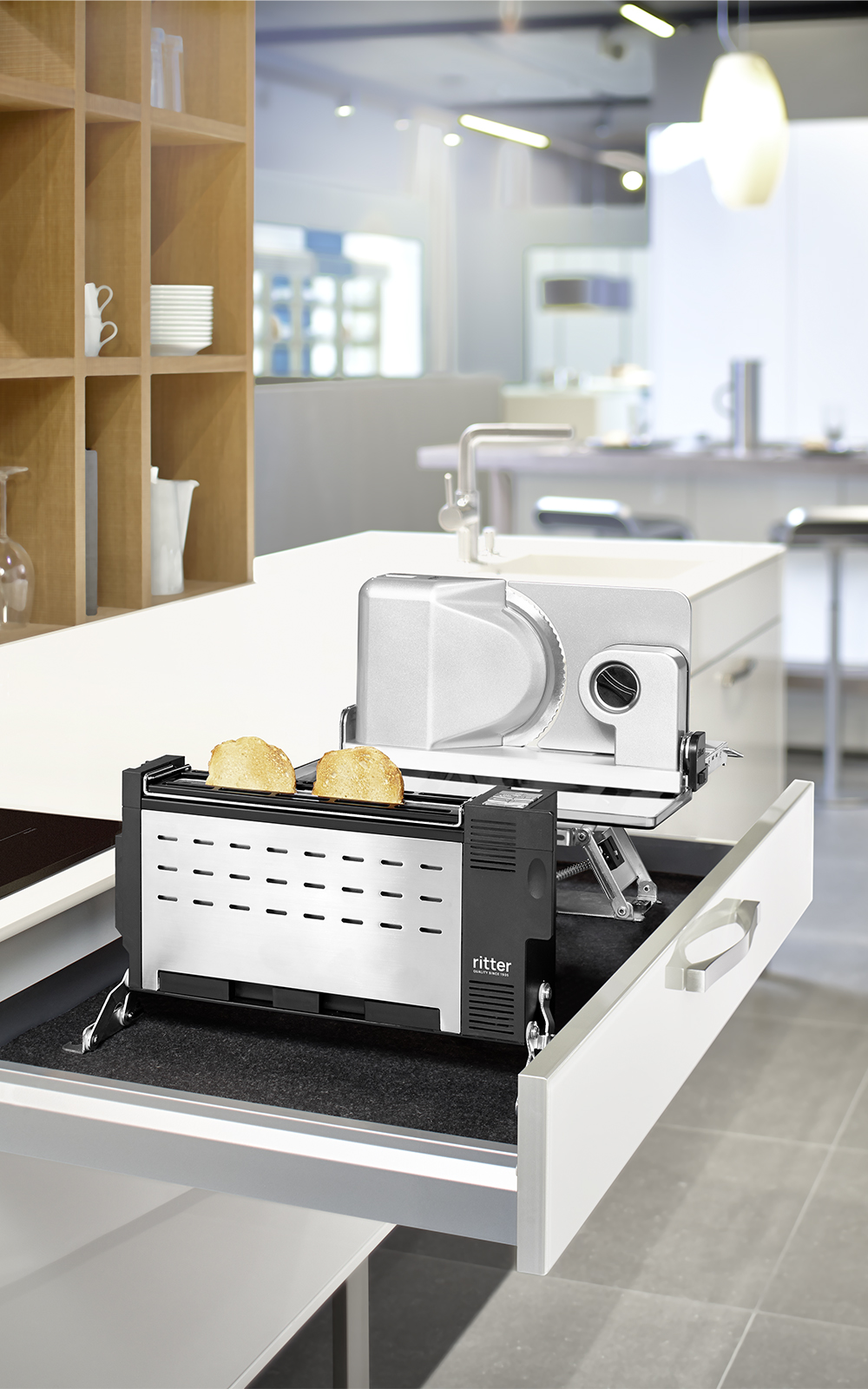 Ein Bild einer Einbaukombination aus einem Einbau-Alleschneider und einem Eibau-Toaster, der Toastbrot toastet, die aus einer Küchenschublade hervorkommt. Ein Bild einer Einbaukombination aus einem Einbau-Alleschneider und einem Eibau-Toaster, der Toastbrot toastet, die aus einer Küchenschublade hervorkommt.