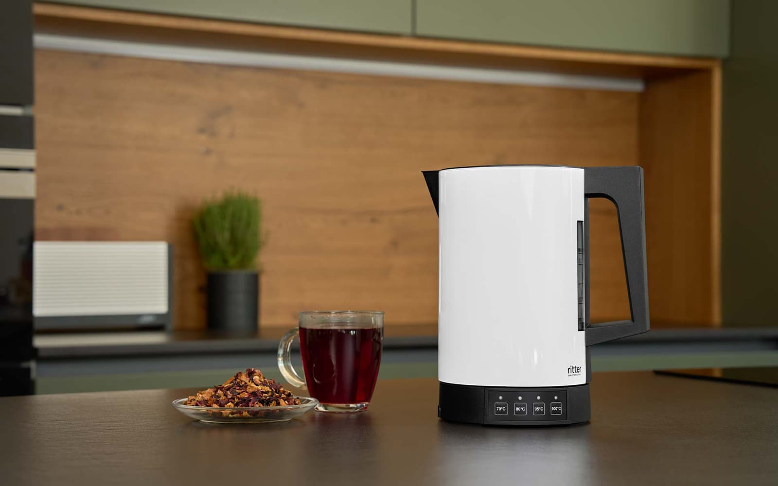 A picture of the white kettle standing on a kitchen platform next to a cup of tea.