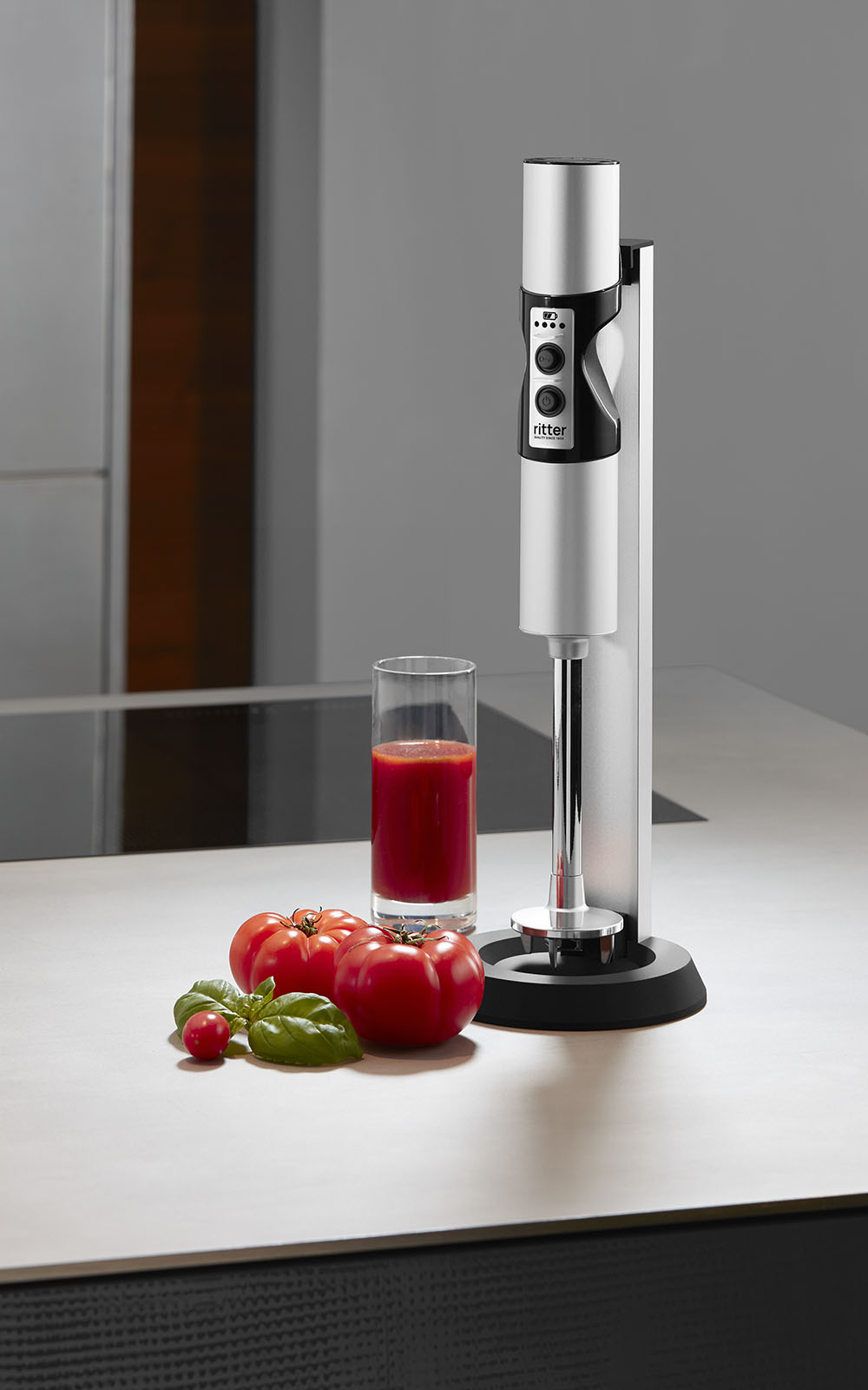 Ein Bild von einem silbernen Stabmixer, der neben einem Glas Tomatensaft, in einer Küche steht. Ein Bild von einem silbernen Stabmixer, der neben einem Glas Tomatensaft, in einer Küche steht.