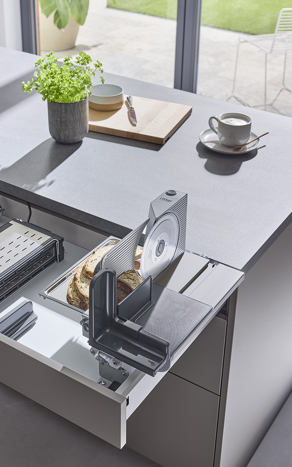 A picture of a built-in food slicer emerging from a kitchen drawer and slicing bread. A picture of a built-in food slicer emerging from a kitchen drawer and slicing bread.