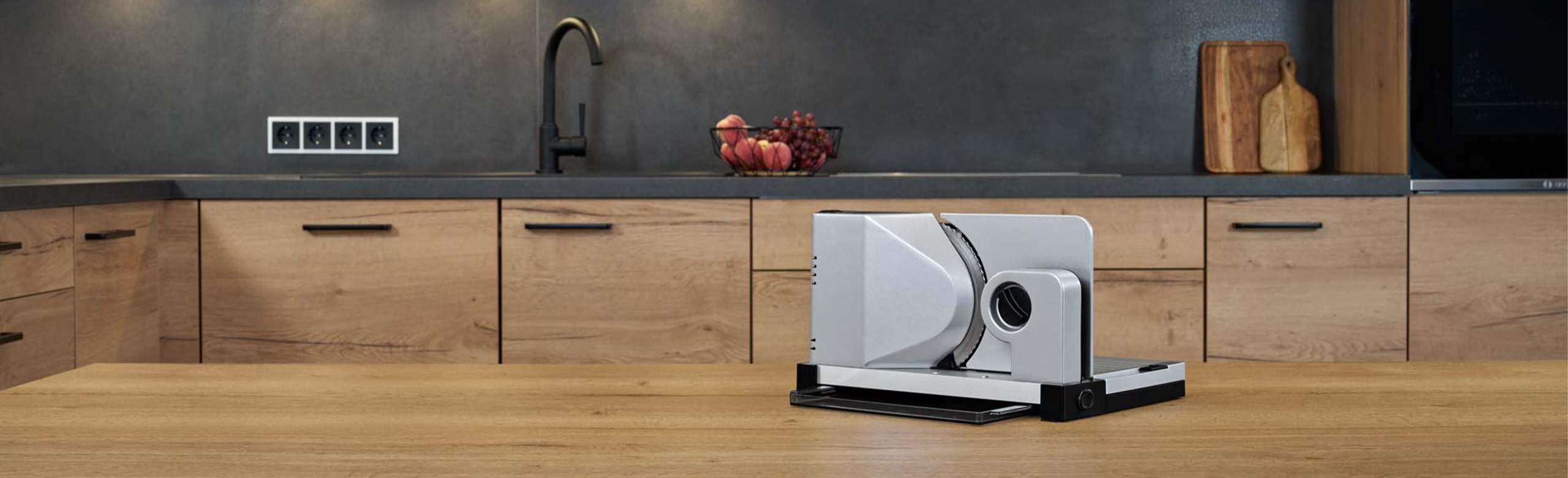 Ein Bild von einem einklappbaren Allesschneider, der auf einer hölzernen Arbeitsfläche in einer Küche steht.