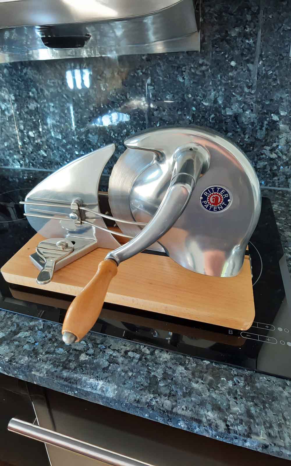 A picture of a manual slicer with a wooden board standing in a kitchen. A picture of a manual slicer with a wooden board standing in a kitchen.